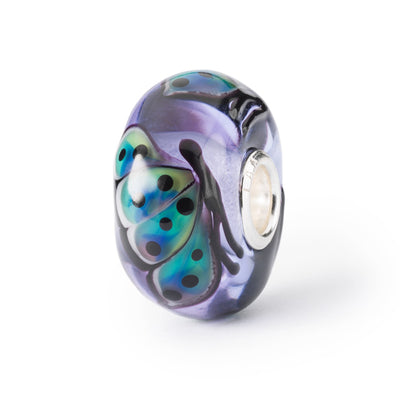 Jewellery bead in glass with colourful butterflies on a light purple background 